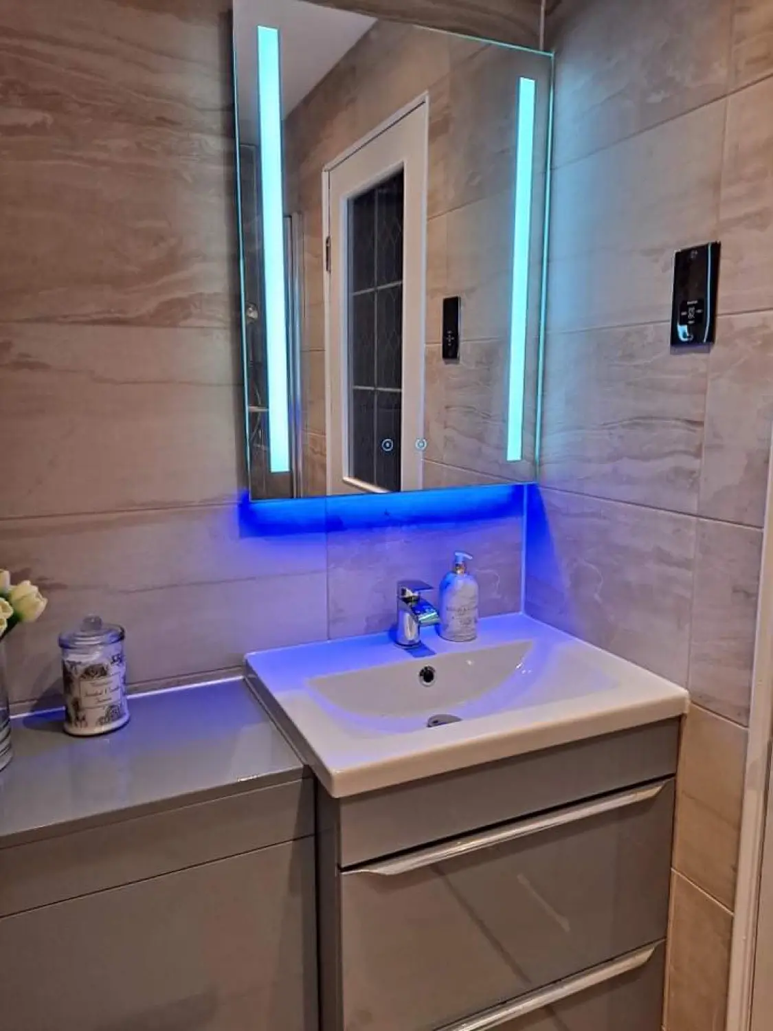 Bathroom vanity unit with basin, tiled walls and an illuminated mirror