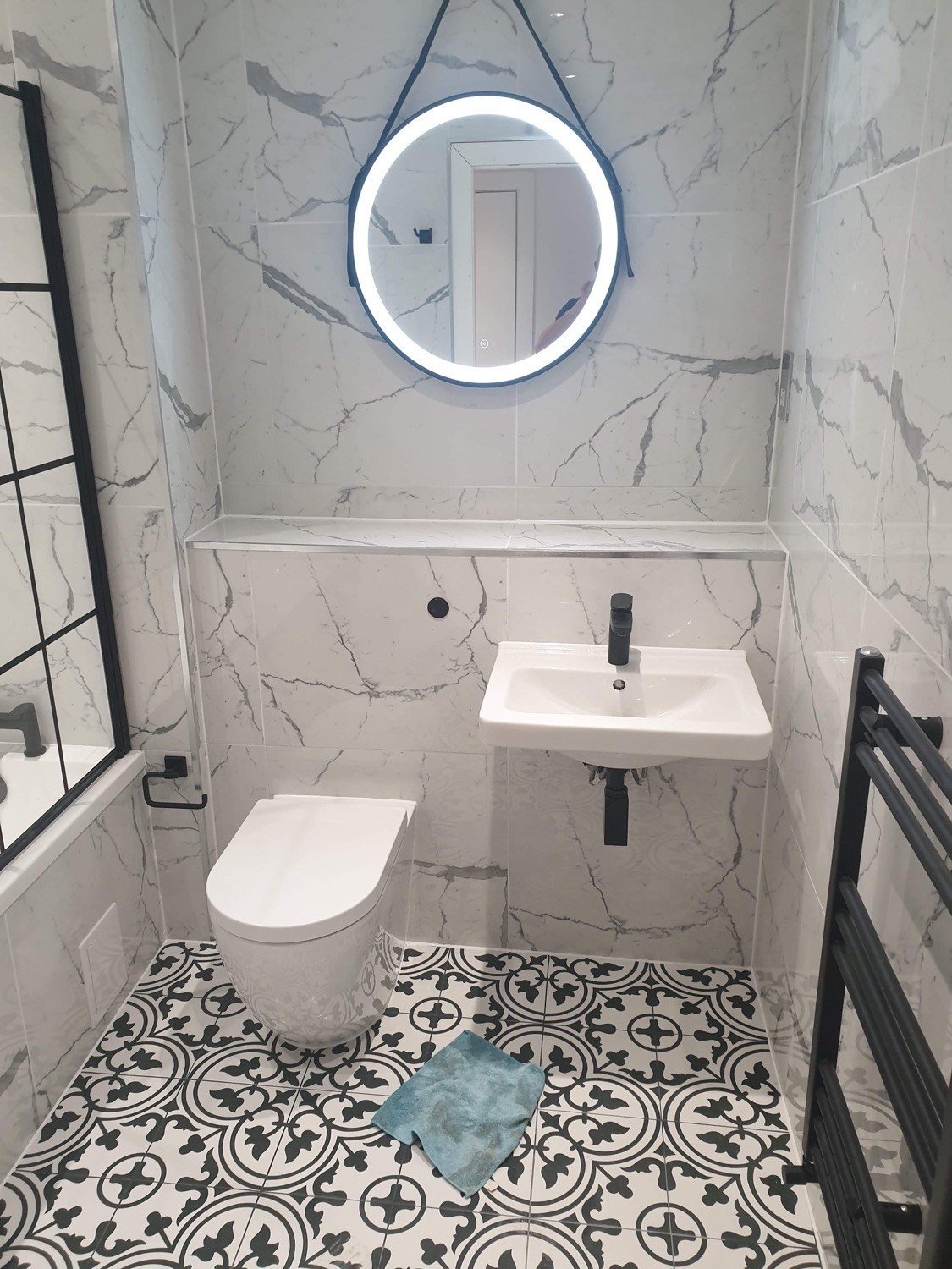 Bathroom with marble-effect wall tiles, patterned floor tiles and a round illuminated mirror